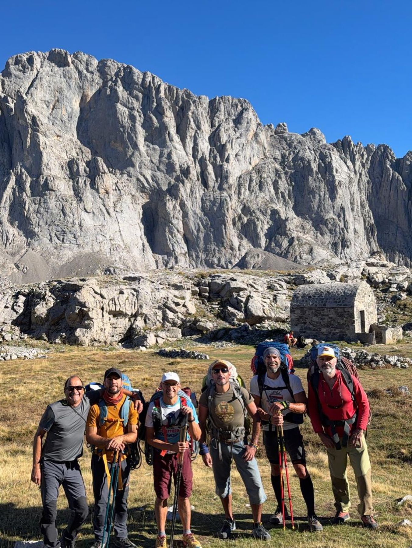 Seis socios sonrientes con mochilas bajo las paredes de Picos de Europa