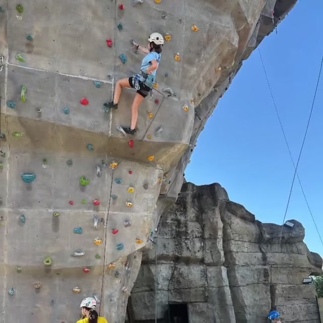 Una niña del taller, con casco y cuerda, escala El Tornillo bajo el cielo azul