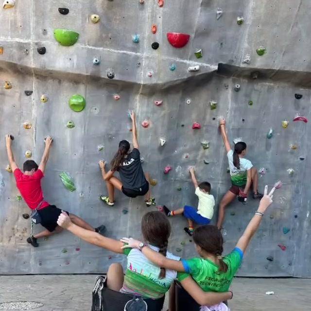 Cuatro niños del taller escalan la pared mientras dos compañeras los animan con los brazos en alto